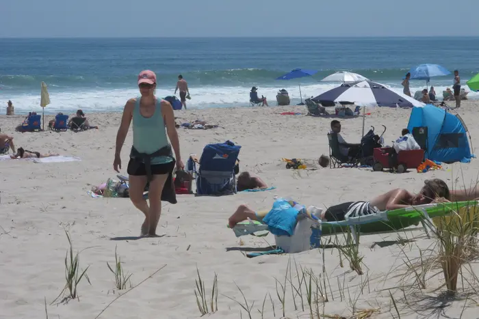 People walk on the beach and people lay on beach chairs and under beach umbrellas by the ocean